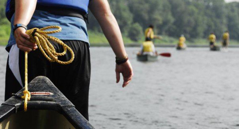 A person pulls a canoe toward the water. There are canoes floating in the background. 